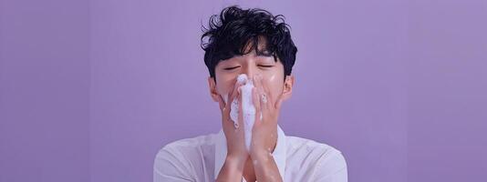 Smiling Asian Man Washing Face in Lavabo with Simple Shirt on Purple Studio Background photo