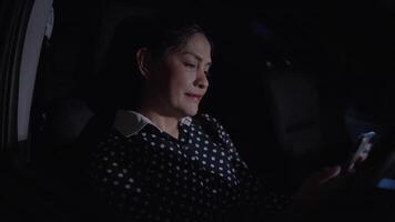 Asian woman sitting in dark car using phone at night. Using smartphone. Looking thoughtful and slightly emotional while reading text message, Darkness, Driving, Stopped for traffic light. Chat message video