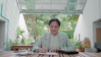 Happy Asian businesswoman working remotely enjoying her job and taking phone calls while taking notes outdoors. Happy and relaxed. Embracing the flexibility of remote work. Data analyst. video