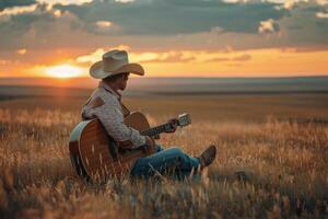 A man in cowboy hat sitting in a field playing guitar photo