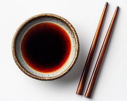 Small dish of soy sauce with chopsticks placed beside it on a white background simple and elegant photo