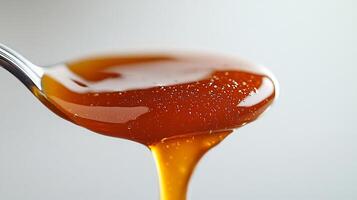 Spoonful of rich caramel sauce dripping onto a white background creating a smooth and glossy texture photo