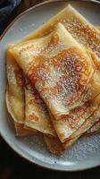 Thin crepes dusted with powdered sugar layered on plate photo