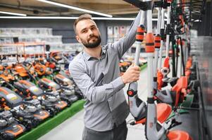 a young man in a gardening equipment store chooses an electric trimmer for mowing lawn grass photo