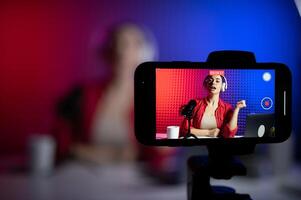 Young attractive woman blogger or vlogger looking at camera and talking on shooting with technology photo