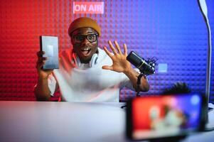 african american vlogger using smartphone to film podcast in studio. blogger with mobile phone, microphone and headphones filming photo