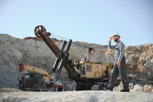 A worker in a helmet stands on the background of an excavator in a quarry photo