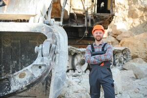 A worker in a helmet stands on the background of an excavator in a quarry photo