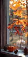 Autumn leaves in glass vase with pumpkins and pine cones on window sill photo