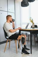 Man amputee with prosthetic leg disability on above knee transfemoral leg prosthesis artificial device using laptop at home. People with amputation disabilities everyday life photo