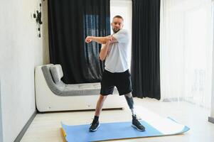 Sporty fit young man amputee with prosthetic leg disability prosthesis doing plank exercise on mat at home. Inclusive sport training for people with disabilities concept photo