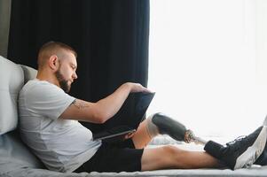 Man amputee with prosthetic leg disability on above knee transfemoral leg prosthesis artificial device using laptop at home. People with amputation disabilities everyday life photo