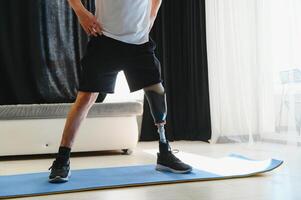 Full length portrait of man with prosthetic leg doing stretching exercises at home and reaching toes photo