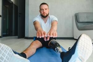 Man amputee with prosthetic leg disability on transfemoral leg prosthesis artificial device making stretching rehabilitation physical exercise at home. People w amputation disabilities everyday life photo