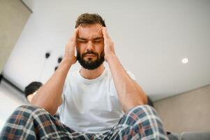 Man suffering from headache at home, touching his temples, copy space, blurred background. Migraine, headache, stress, tension problem, hangover concept photo