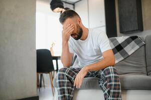 Man suffering from headache at home, touching his temples, copy space, blurred background. Migraine, headache, stress, tension problem, hangover concept photo