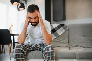 Man suffering from headache at home, touching his temples, copy space, blurred background. Migraine, headache, stress, tension problem, hangover concept photo
