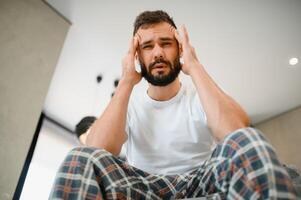 Man suffering from headache at home, touching his temples, copy space, blurred background. Migraine, headache, stress, tension problem, hangover concept photo