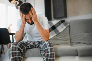 Man suffering from headache at home, touching his temples, copy space, blurred background. Migraine, headache, stress, tension problem, hangover concept photo