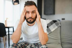 Man suffering from headache at home, touching his temples, copy space, blurred background. Migraine, headache, stress, tension problem, hangover concept photo