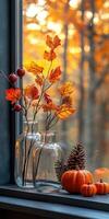 Autumn leaves in glass vase with pumpkins and pine cones on window sill photo