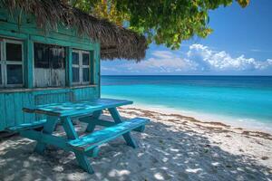 Empty blue picnic table on the beach in front of a beach shack overlooking turquoise water photo