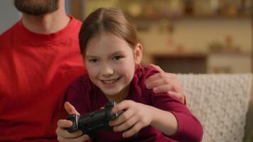 Caucasian family playing game addict child kid little girl play online console with dad adult man father support parental control daughter play joystick gaming addiction gamer on couch at home video