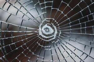 Shattered glass with radial cracks, forming a spiderweb pattern, faint background photo