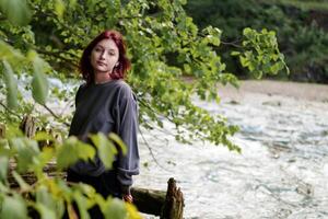 Confident, free-spirited zomer stands tall, her alternative aesthetic complemented, atmospheric backdrop of a flowing river and dense greenery photo