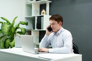 focused young man is actively discussing a project over the phone while working at a computer in a modern office environment photo
