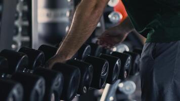 Overweight guy taking dumbbells for weightlifting exercise, using professional equipment at gym, close up, slow motion video