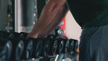 Close up view on overweight man taking dumbbells from rack at gym, slow motion video