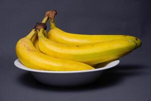 A banch of bananas and a sliced banana in a plate over brownd background. photo