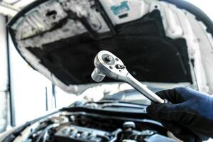 Mechanic is repairing a car engine , Auto mechanic hand holds a socket wrench with blurred car engine compartment in the background , car repair concept photo