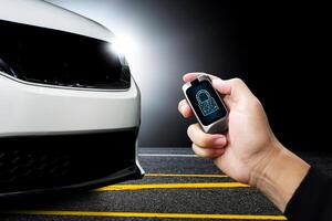 Driver hand holds keyless remote with key locked icon on display with white modern car parked on the road in the background , Technology concept for preventing car theft photo