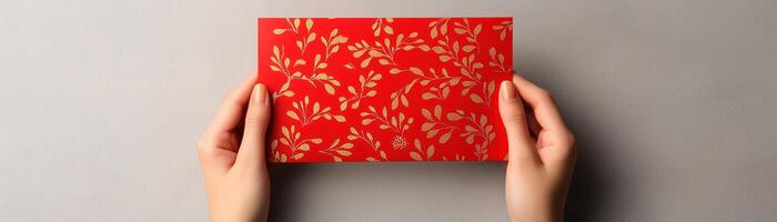 A pair of hands holding a vibrant red envelope with a floral pattern against a neutral background, perfect for invitations and special occasions. photo