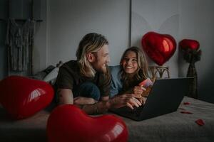 Happy loving couple using laptop and credit card while shopping online at Valentines day photo