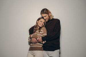 Fashionable young loving couple in cozy warm wear embracing while standing on beige background photo