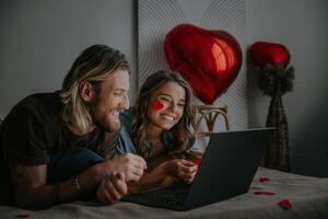 Joyful loving couple looking at laptop and using credit card while shopping online at Valentines day photo