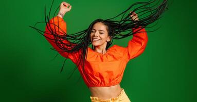 Attractive young woman with dreadlocs dancing and looking happy against green background photo