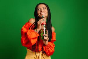 Attractive young woman enjoying fresh lemonade and smiling against green background photo