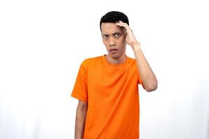 Portrait of a young Asian man wearing an orange t-shirt looking surprised, shocked and shocked. Hands are near eyes, isolated on white background. photo