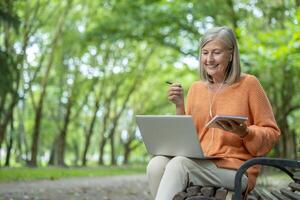 Smiling woman learning online in a serene outdoor environment using laptop and notebook. Capturing knowledge and nature, she enjoys the synergy of technology and tranquility for productive learning. photo
