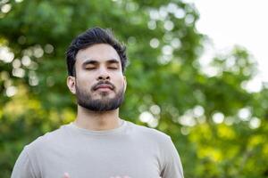 Young man engages in mindfulness and relaxation exercises, standing outdoors with eyes closed. Captures peaceful moments of meditation and wellness, highlighting focus on breathing photo