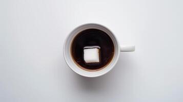 Lone sugar cube rests on the surface of a cup of black coffee in a white mug on a clean white table photo