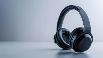 Wireless black headphones with earcups resting on a table against a pale gray backdrop photo