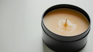 Soy wax candle in a black tin is slowly melting, forming a pool of liquid wax around the wick photo