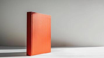 Orange hardcover book standing upright on white surface with gray wall in background photo