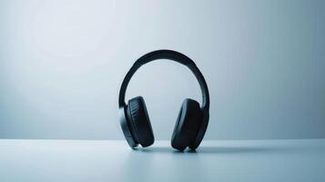 Black wireless headphones are placed on a white table with a light blue background photo