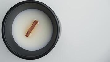 Wooden wick floating in scented candle wax inside a black container on white surface photo